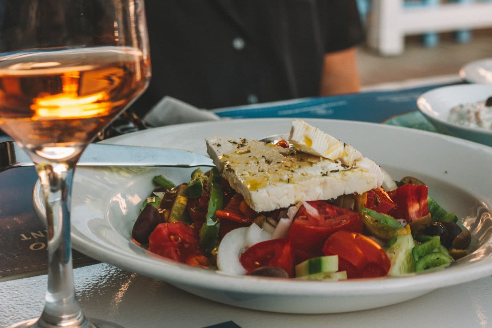 A Greek salad topped with feta next to a glass of wine