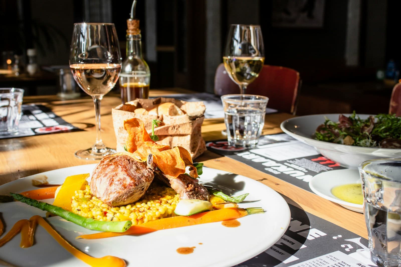 A plated dinner with glasses of wine on a sunlit restaurant table
